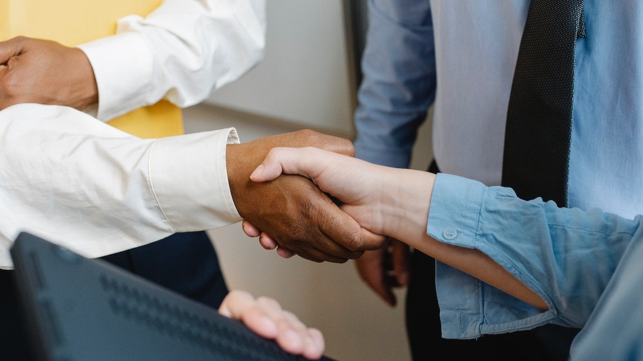 Multiracial colleagues shaking hands at work | Goodwill Car Donations