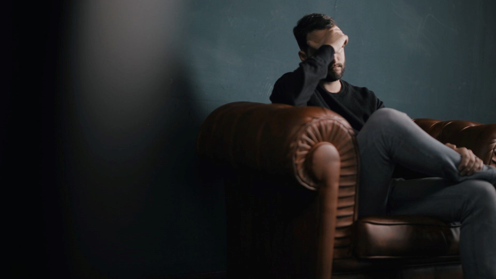 a man holds his head while sitting on a sofa photo | Goodwill Car Donations