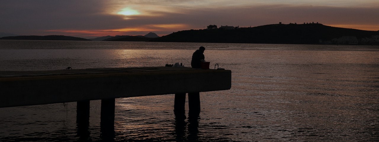 Silhouette of a Person Sitting on Concrete Dock during Sunset | Goodwill Car Donations