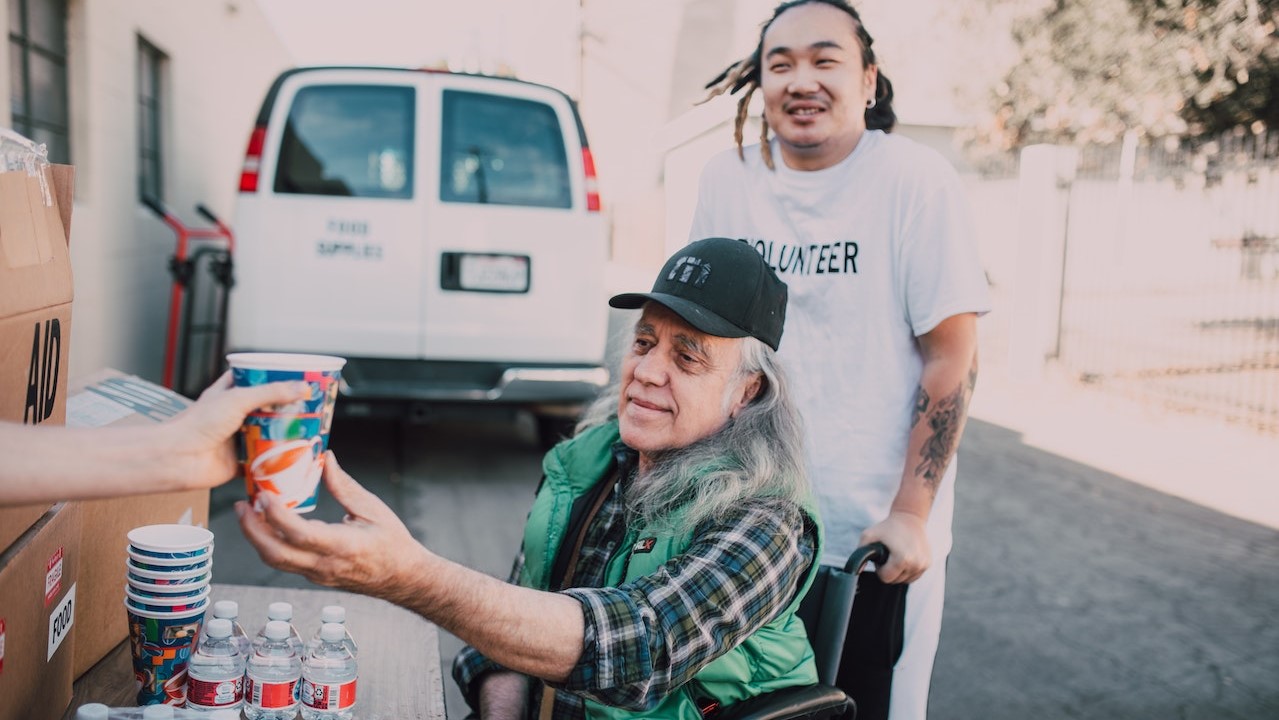 Volunteers Giving Drink to a Wheelchair Bound Elderly | Goodwill Car Donations