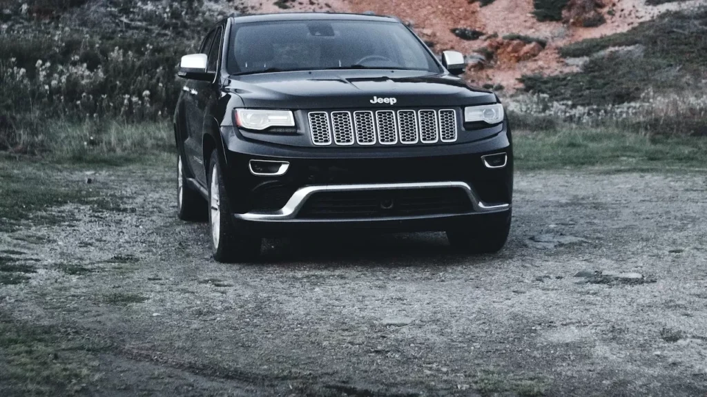 A black SUV is parked on a dirt road against a rugged rocky hillside