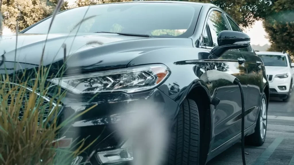 A black hybrid car charging at an outdoor station surrounded by greenery