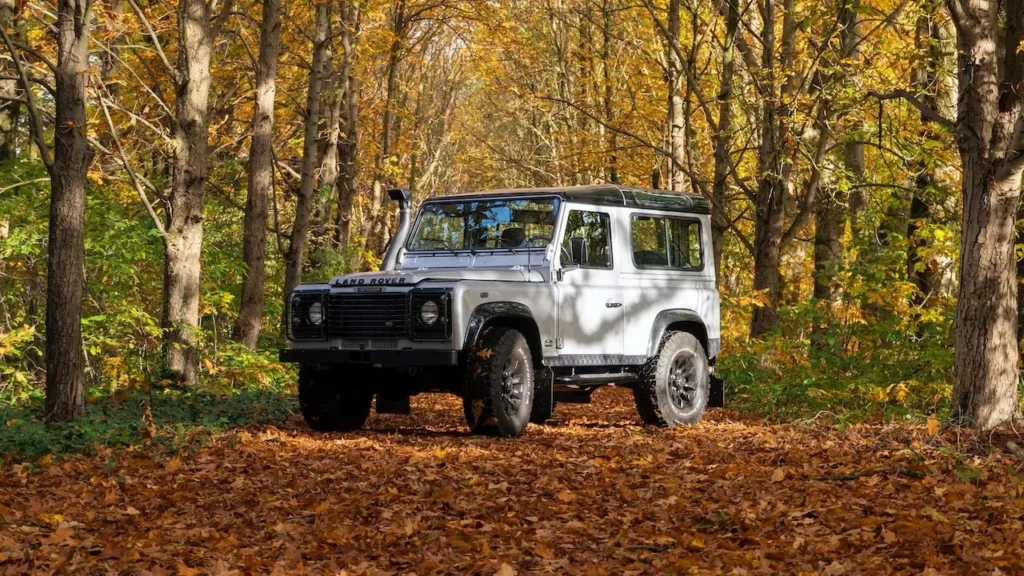 A Land Rover Defender parked in a vibrant autumn forest with fall foliage
