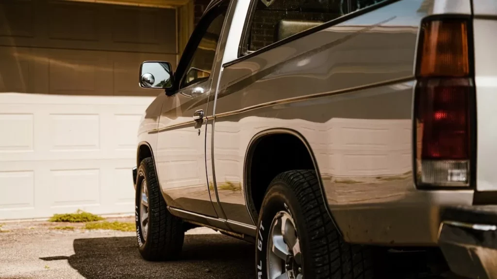 A silver pickup truck parked in a sunny residential driveway with closed garage doors