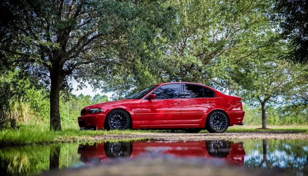 A stunning red classic car parked beside a serene lake surrounded by lush greenery