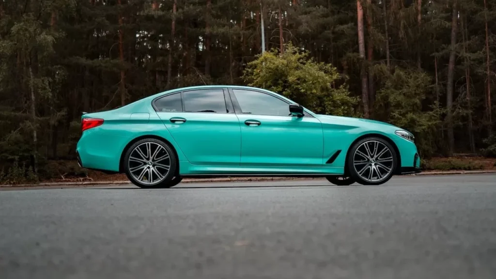 A vibrant green sedan parked on a road amidst a dense forest, showcasing modern automotive elegance