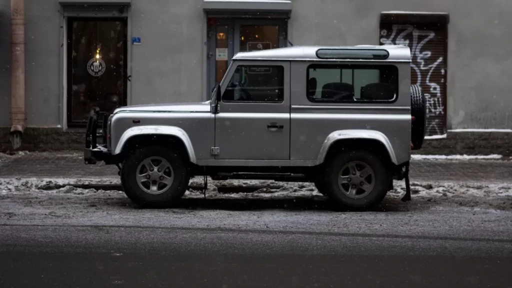 A silver SUV parked by a snowy city street near a cafe.