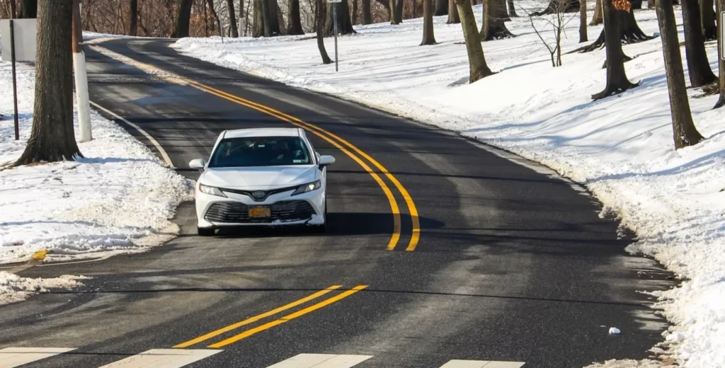 A white car driving down a snow covered road