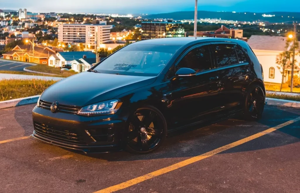 A modern black car parked in an urban setting at twilight with a cityscape background