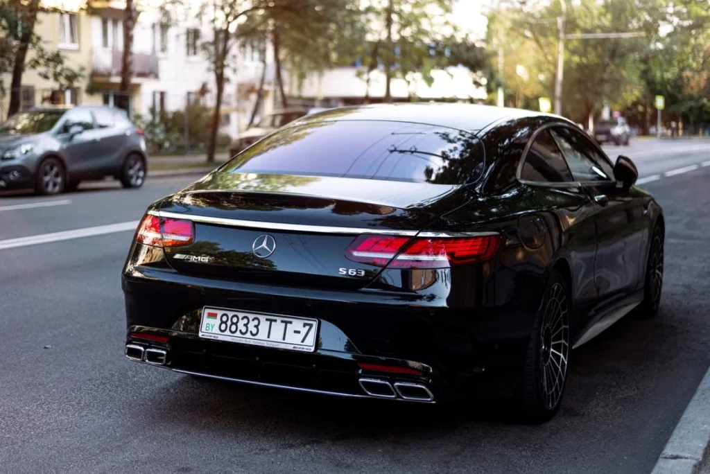 Sleek black luxury car parked on a city street with sunlight reflecting off its surface