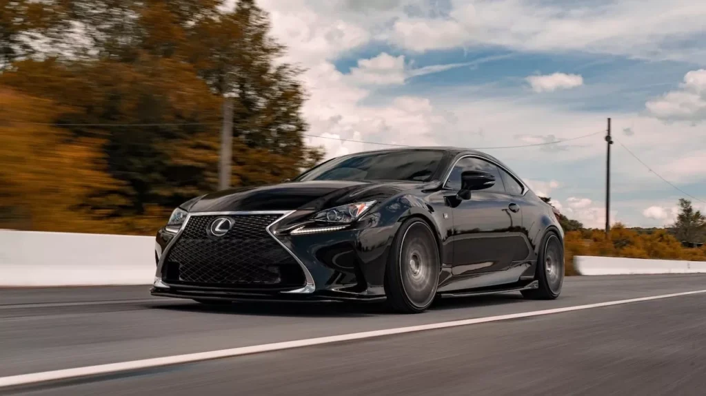 A black luxury car driving swiftly on an open road amidst scenic landscapes and clear skies