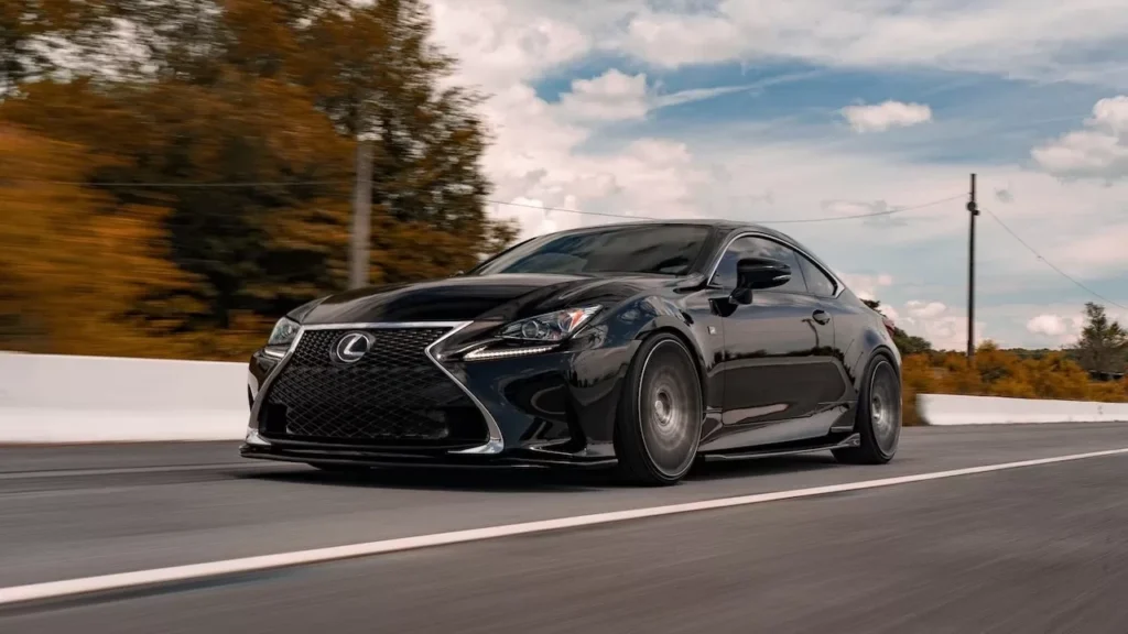 A black luxury car driving swiftly on an open road amidst scenic landscapes and clear skies