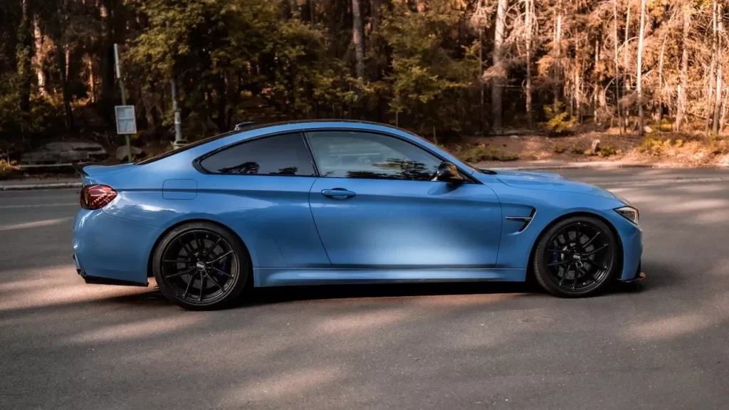 Blue sports car parked on asphalt road beside a forest area, capturing automotive elegance.