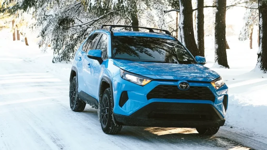 A shiny blue SUV parked on a snow-covered forest road on a bright winter day