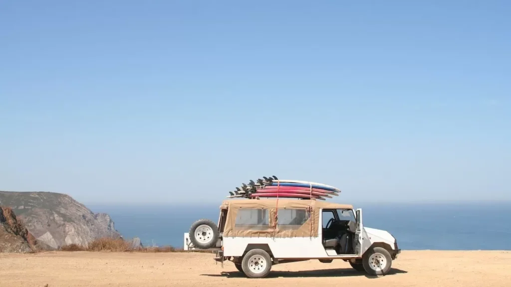 A jeep loaded with surfboards parked by a scenic ocean cliff under a clear sky
