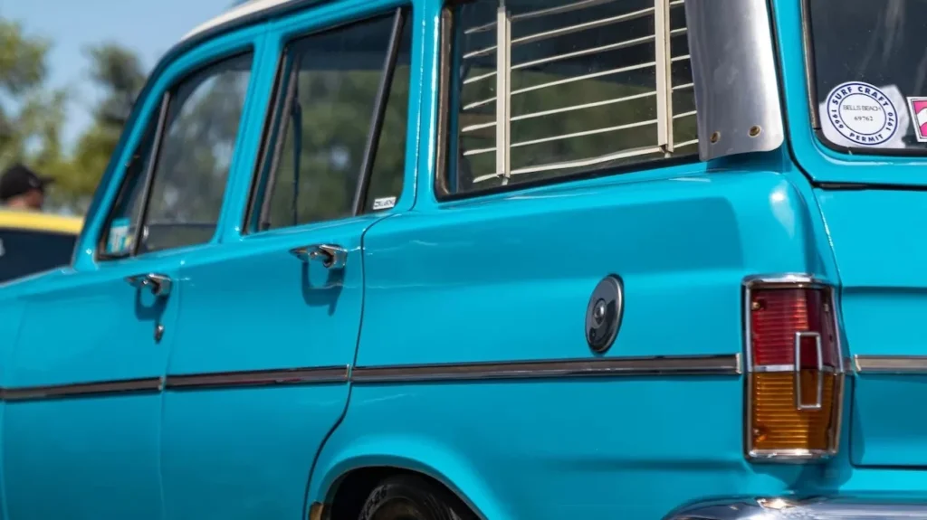 Bright blue vintage car parked with clear skies and trees, showcasing classic design