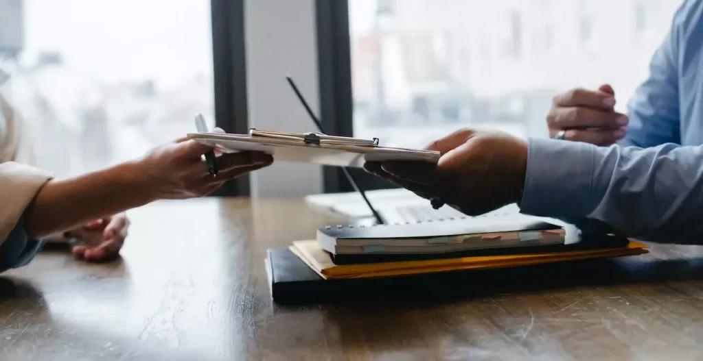 Hands exchanging documents during a professional meeting in an office environment.