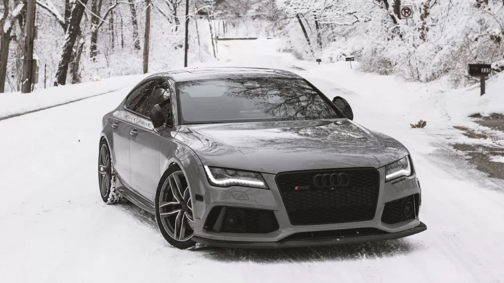 A sleek luxury car parked on a snow-covered road surrounded by winter trees