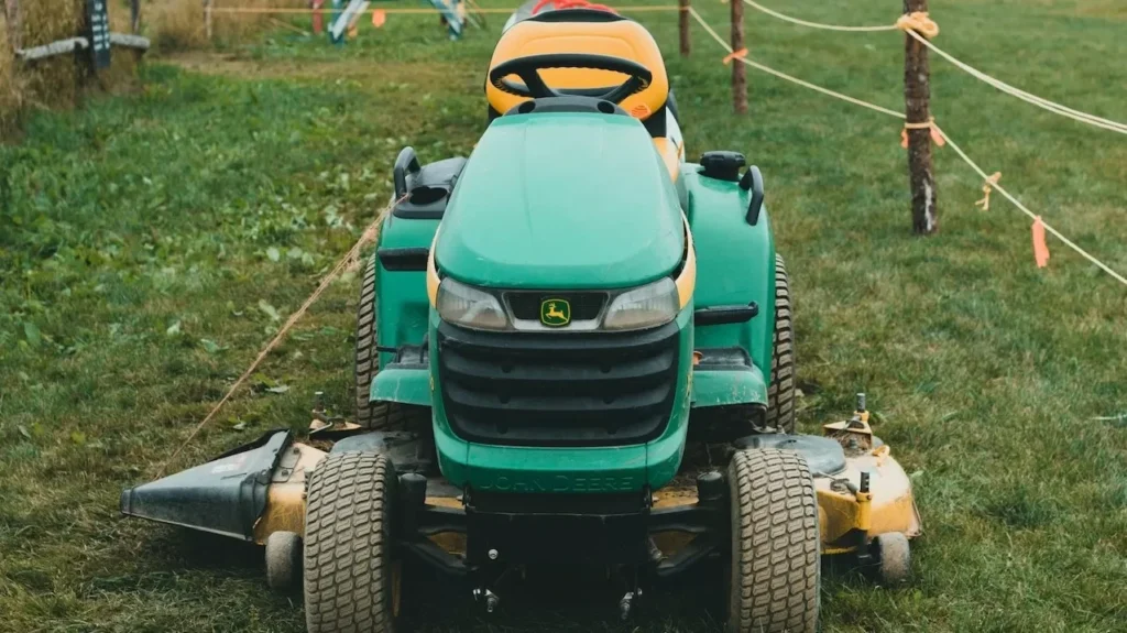 green riding lawn mower sits on a vast grassy field with rustic fencing in a tranquil rural setting.