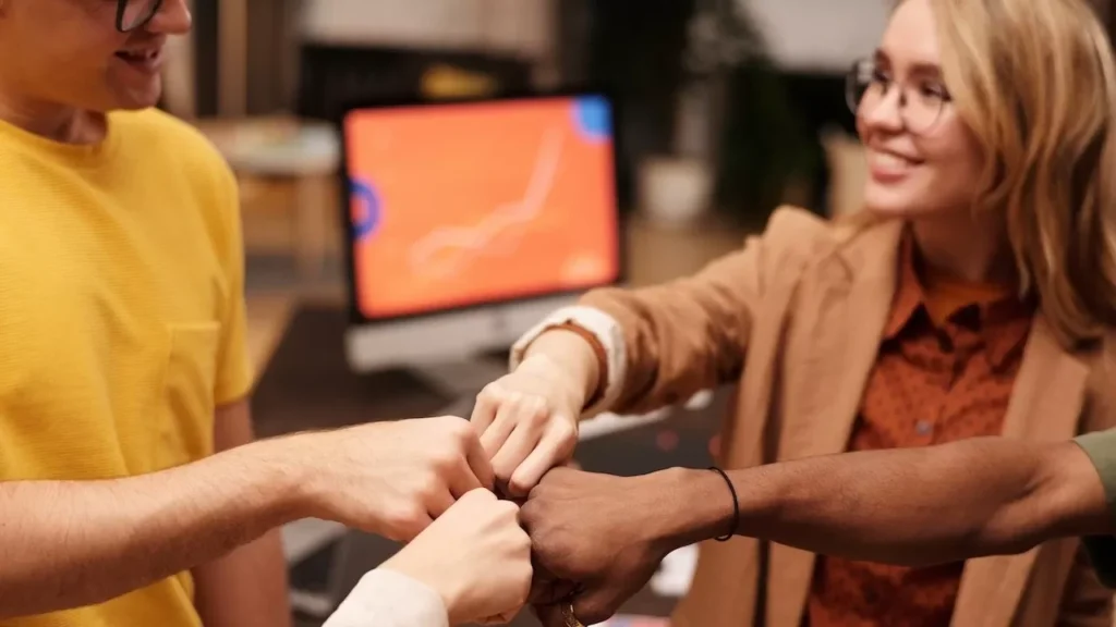 Group of colleagues fist bumping to celebrate teamwork and unity in a modern office setting