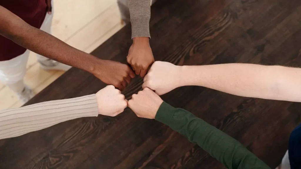 view of diverse hands fist bumping on wooden table, symbolizing teamwork, unity, and cooperation.