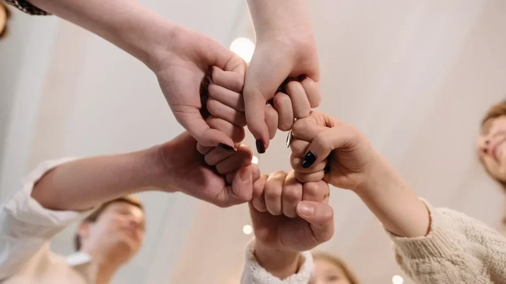 a diverse group joining fists in a show of unity and teamwork indoors.