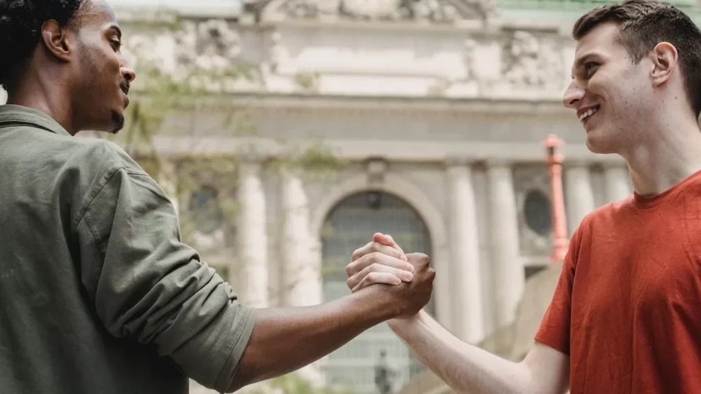 friends share a joyful handshake in an urban setting, capturing a moment of friendship and positivity.