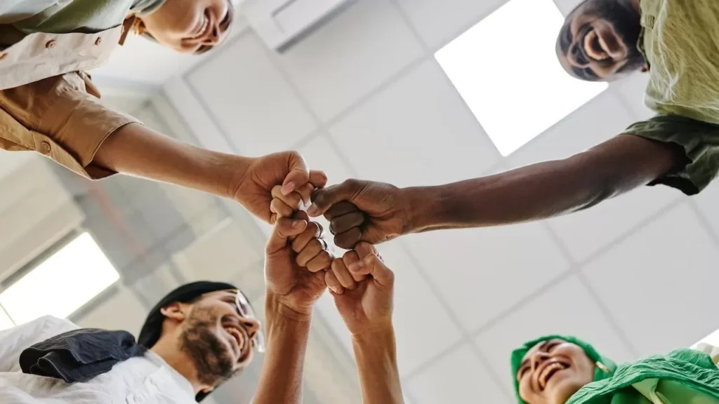 A diverse group of colleagues perform a fist bump in an office setting, symbolizing teamwork.