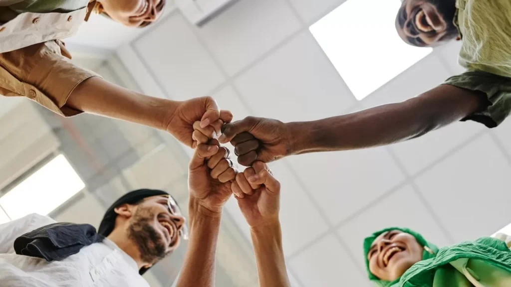 diverse group of colleagues perform a fist bump in an office setting, symbolizing teamwork.