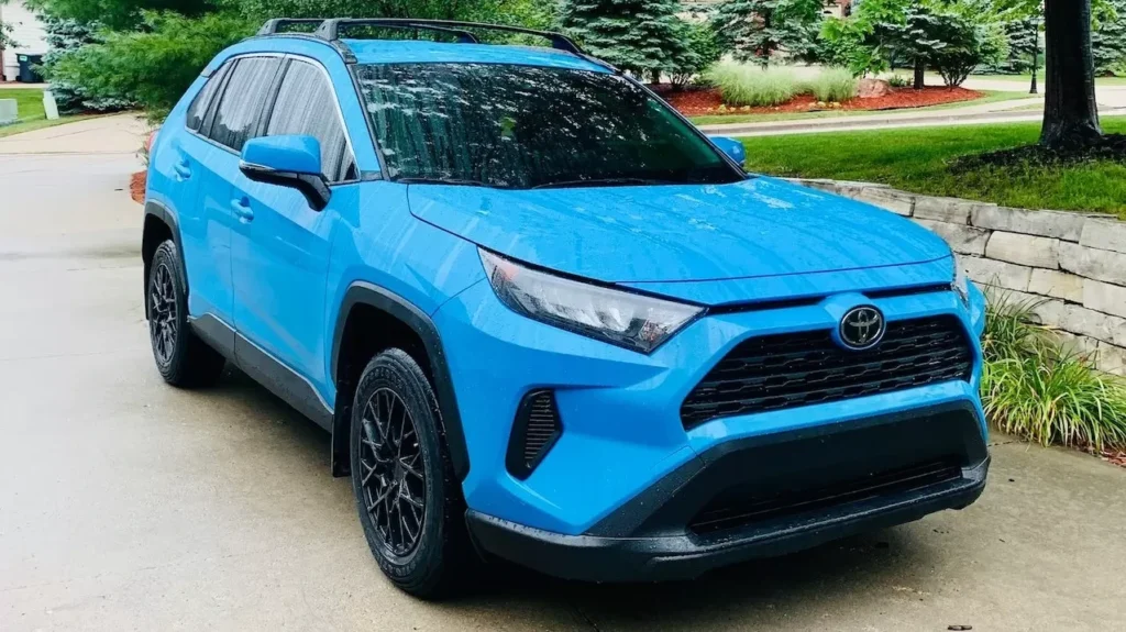 Bright blue SUV parked on a driveway surrounded by lush greenery on a cloudy day.