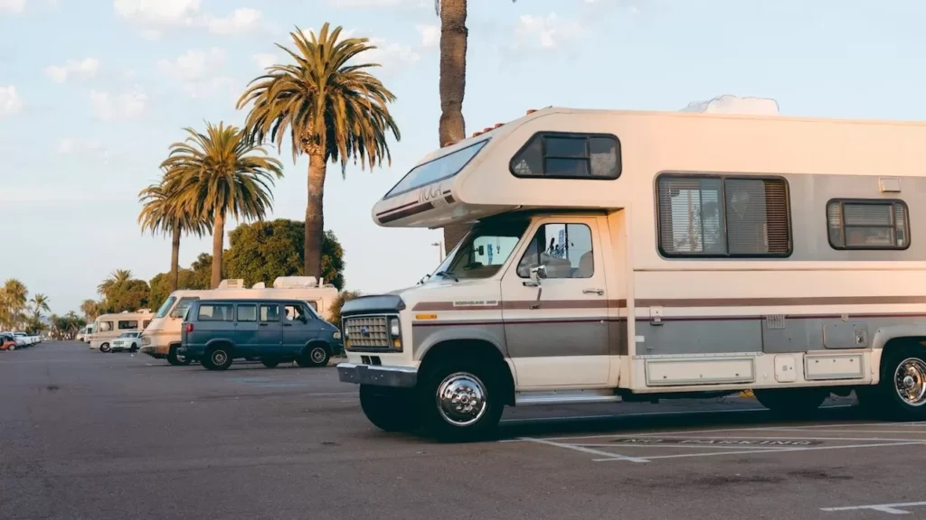 RVs parked under palm trees in a bright daylight urban parking lot setting