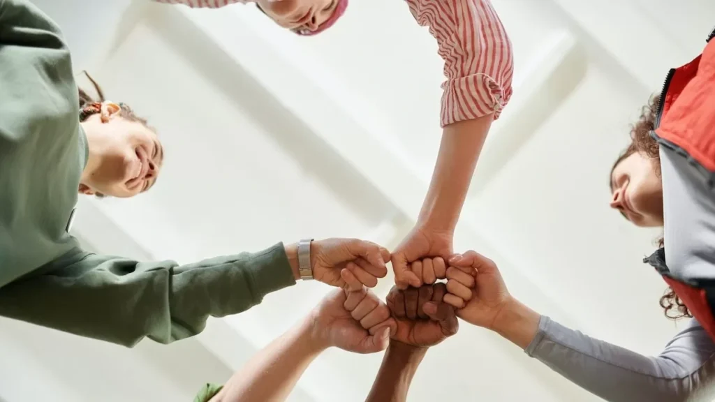 Four diverse team members join fists together, displaying unity and teamwork