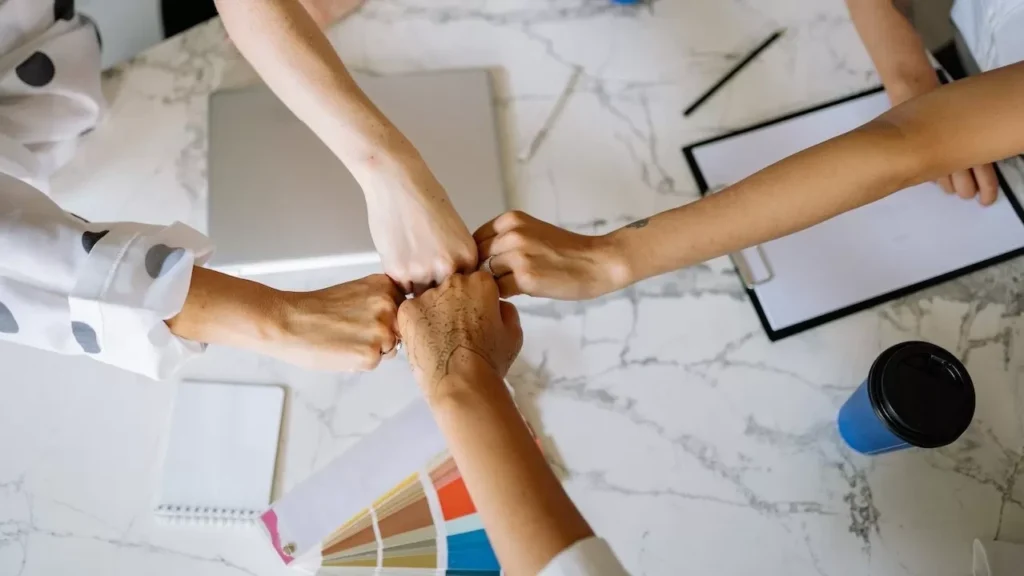view of diverse team members fist bumping over a marble table in a collaborative office setting