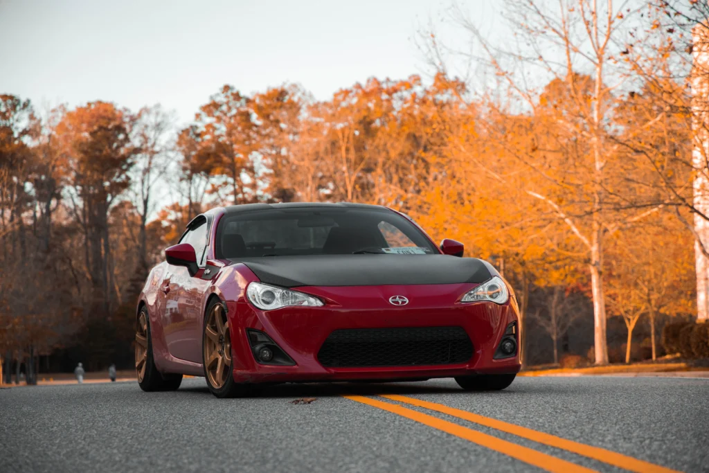 A vibrant red sports car parked on a scenic autumn road with golden foliage