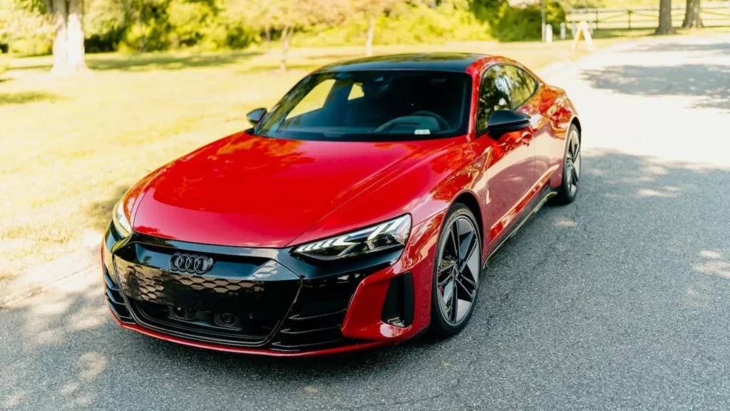 A sleek red luxury electric car parked under bright sunlight on a paved road