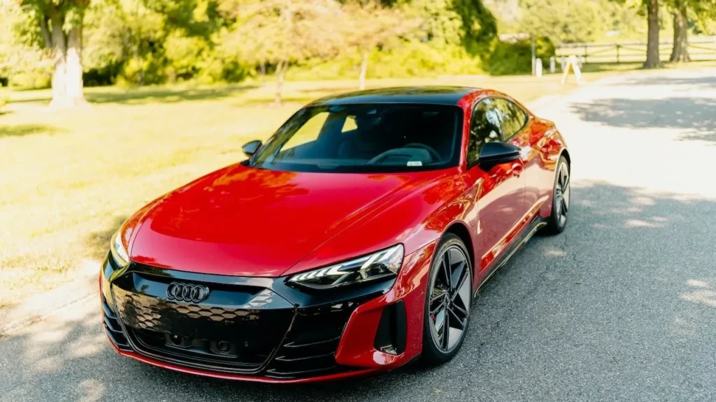 A sleek red luxury electric car parked under bright sunlight on a paved road