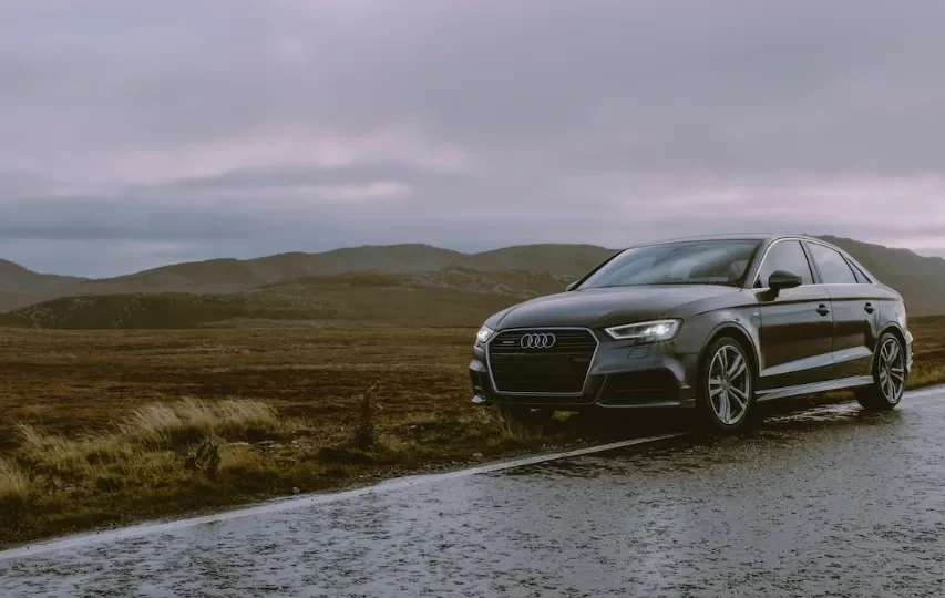 A luxury Audi sedan parked on a wet mountain road with moody skies and a scenic backdrop