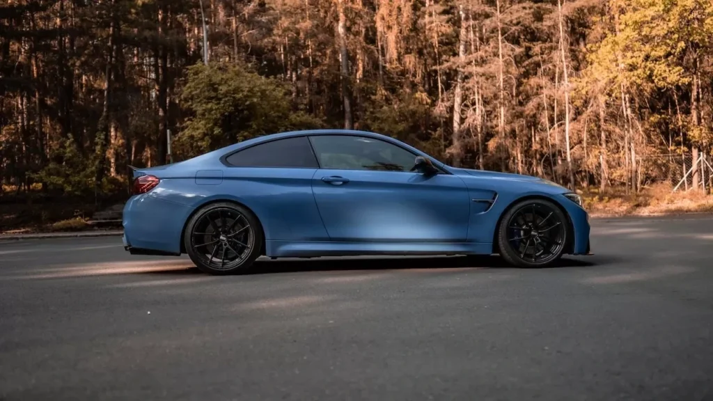 Blue luxury sports car parked on a forest road, side view with natural sunlight casting shadows