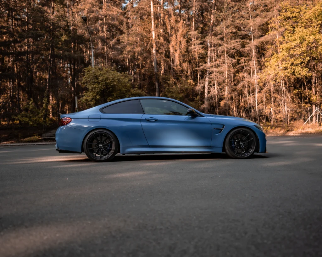 Blue luxury sports car parked on a forest road, side view with natural sunlight casting shadows