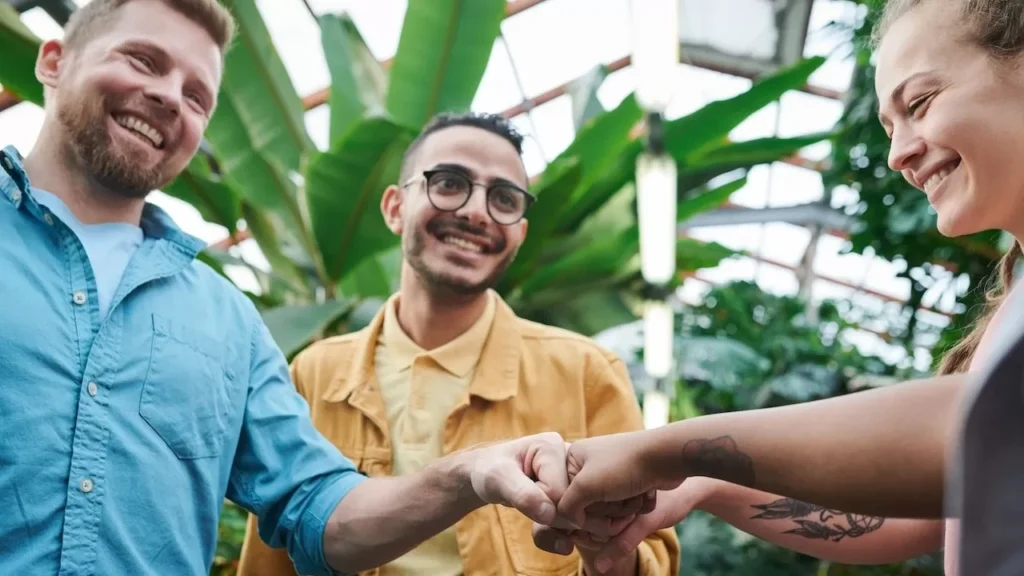 Three friends sharing a joyful fist bump in a lush indoor greenhouse environment