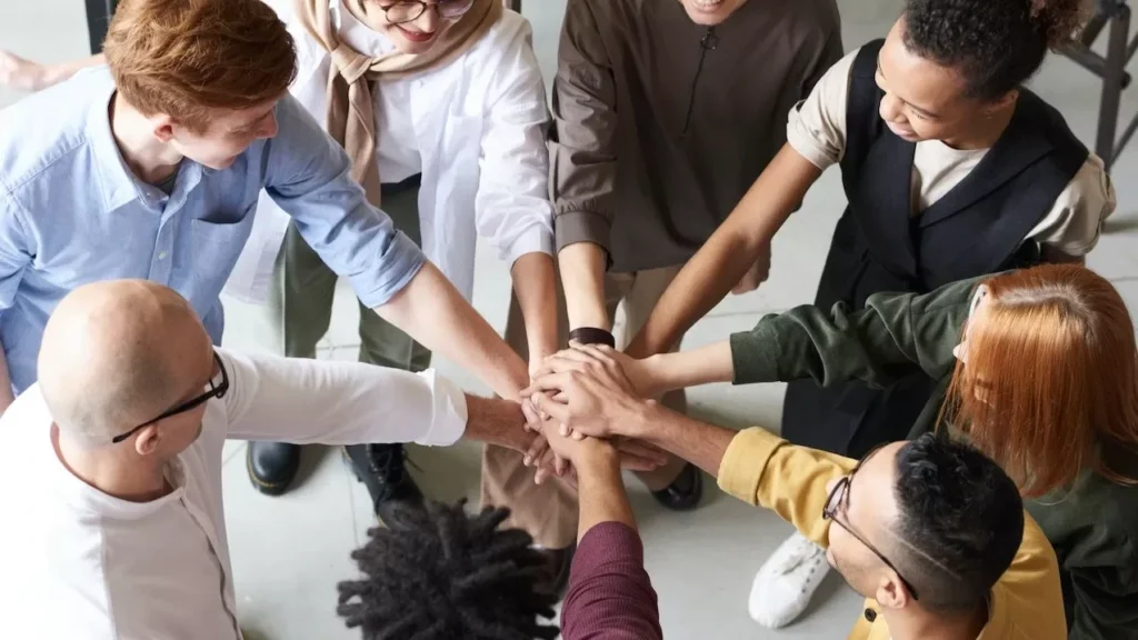 A diverse group of professionals joins hands in a team-building exercise indoors