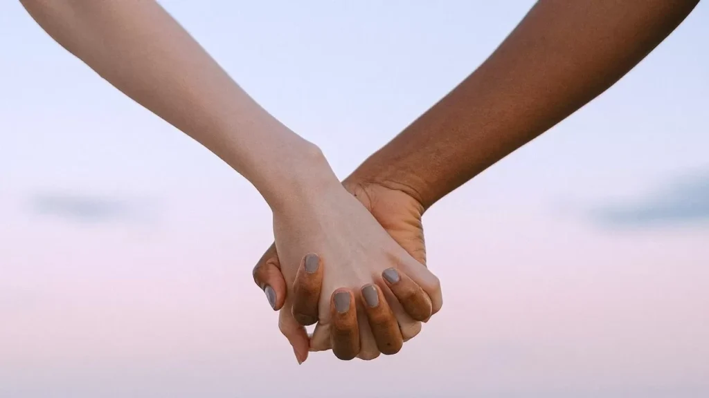 Closeup of multiracial hands holding, symbolizing unity and equality against a serene sky