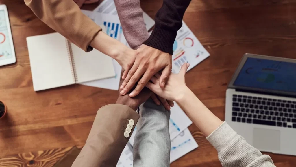 Diverse professionals unite for teamwork around a wooden table with laptops and documents