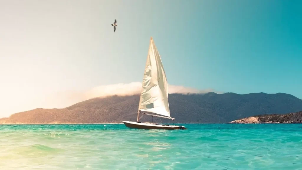 A sailboat glides across turquoise seas beneath a clear sky