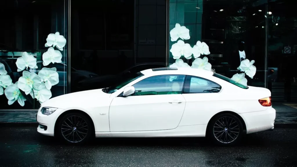 A stylish white coupe car parked outdoors with floral window display background.