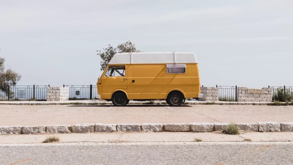 A classic yellow van parked by a scenic seaside road in Sardinia, Italy, under a clear sky