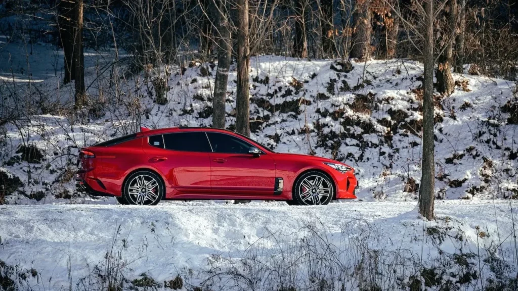 A sleek red car parked in a snowy forest, depicting a serene winter scene