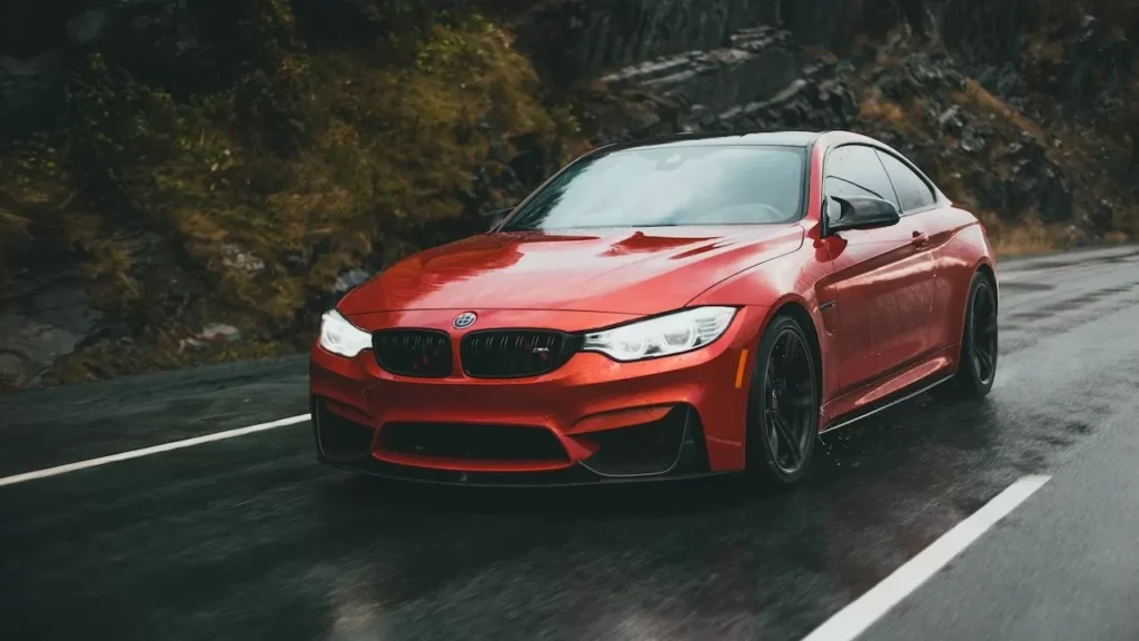 A sleek red sports car driving on a wet road under cloudy skies, showing speed and luxury