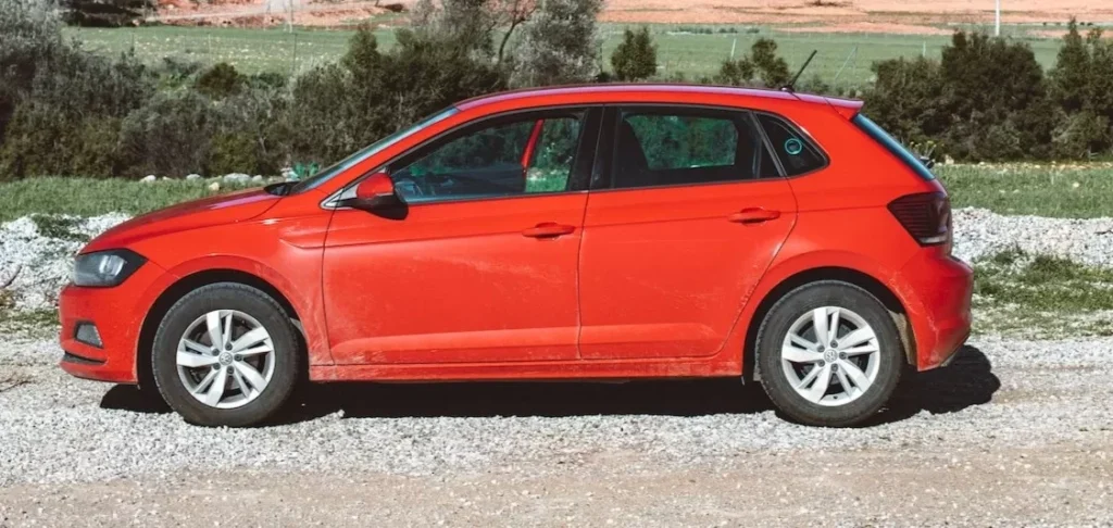 ibrant red car parked against a beautiful countryside backdrop with clear blue sky