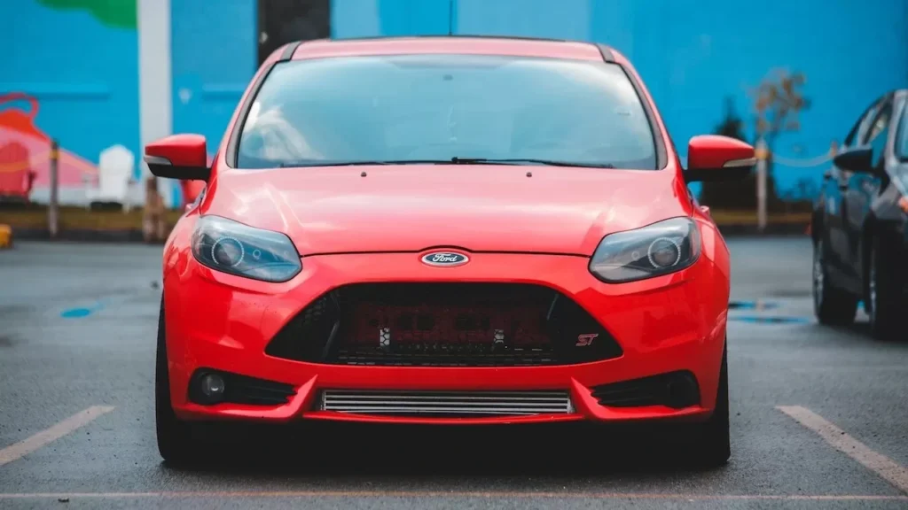 A bright red Ford car parked on a city street on a cloudy day